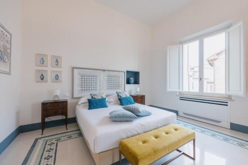 a white bedroom with a large bed with blue pillows at Dimora Dell'Erbe Apartments in Montepulciano