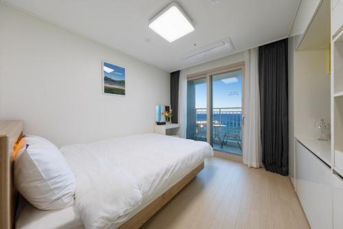 a white bedroom with a bed and a balcony at Yangyang Badastay in Yangyang