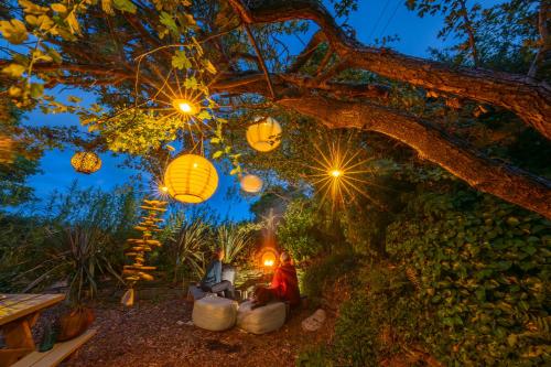 a woman sitting under a tree with lanterns at The Paddock Wildcamp in Perranporth