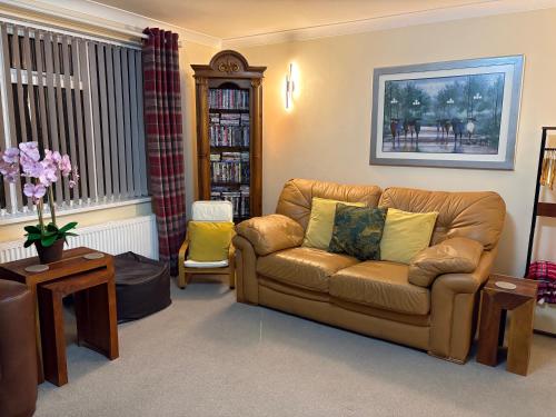 a living room with a leather couch and a book shelf at Acorn Cottage in Ollerton