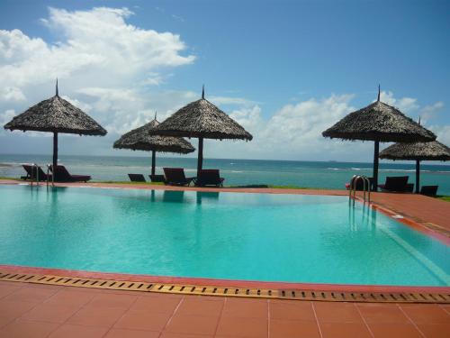 a swimming pool with umbrellas and chairs and the ocean at Amani Beach Resort in Dar es Salaam