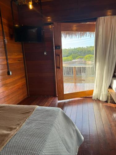 a bedroom with a door open to a deck with a view at AREIA BRANCA Chalés in Santo Amaro