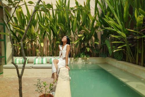 a woman in a white dress sitting next to a swimming pool at Kuka y Milpa in Mérida