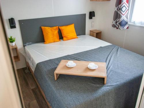a bed with yellow pillows and a wooden table at MOBIL-HOME "B27" tout confort avec piscine & lave-linge gratuits in Mimizan