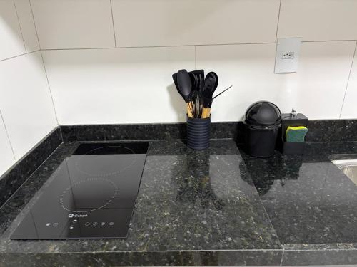 a kitchen counter with a black counter top with utensils at Residencial Bom Sossego Apto 01 in Itabuna