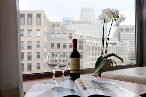 a bottle of wine and two glasses on a table with a window at Canary Riverside Plaza Hotel in London