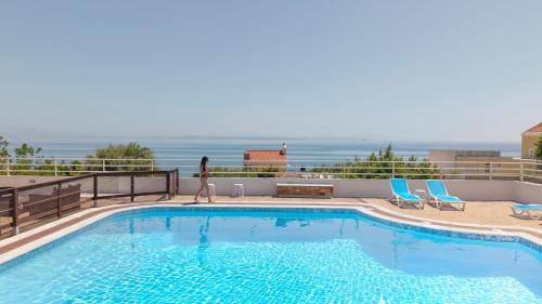 a woman walking by a swimming pool with the ocean in the background at CHIOS HOTEL in Katarráktis
