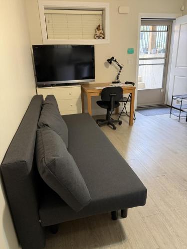 a couch in a living room with a desk and a television at Garden suite in Vancouver