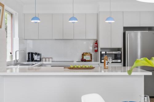 a kitchen with white cabinets and a stainless steel refrigerator at Fathoms 13 Mollymook Beach in Mollymook
