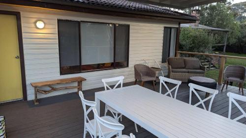 a deck with white chairs and tables and a window at Sandy's Beach Shack at Bawley in Bawley Point