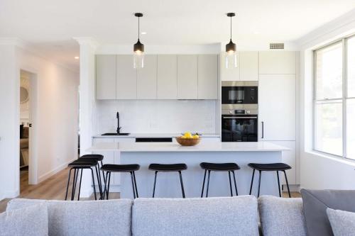 a white kitchen with a couch and some bar stools at Mollymook Delight - with easy ocean & golf access in Mollymook
