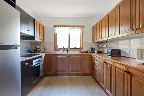 a large kitchen with wooden cabinets and a window at Barker Retreat in Burrill Lake