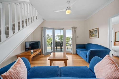 a living room with blue couches and a tv at Bowen View - pet-friendly home near Hyams Beach in Hyams Beach