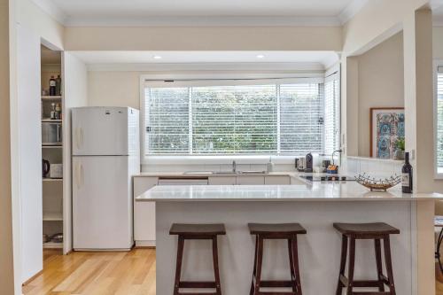 a kitchen with a white refrigerator and two bar stools at Bowen View - pet-friendly home near Hyams Beach in Hyams Beach