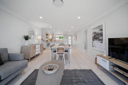 a living room with a couch a table and a tv at Days By The Bay - 3BR house with ocean views in Hyams Beach