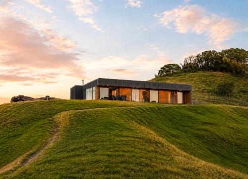 a house on top of a grassy hill at Ocean Waters in Mahia