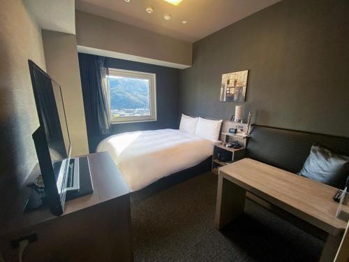 a hotel room with a bed and a desk with a television at Hotel Route-Inn Tsuyama Ekimae in Tuyama