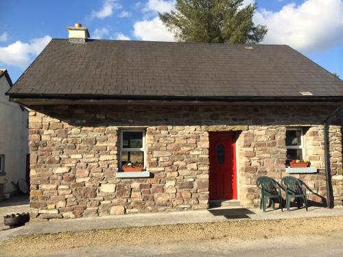 a stone building with a red door and chairs at Douglas Lodge Holiday Homes in Keadew
