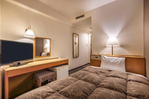 a hotel room with a bed and a desk with a television at Az Inn Fukui (Ace Inn Fukui) in Fukui