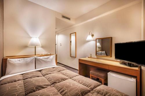 a hotel room with a bed and a desk with a television at Az Inn Fukui (Ace Inn Fukui) in Fukui