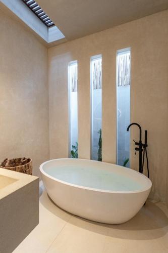 a large white bath tub in a bathroom with windows at Heritage Villas in Uluwatu