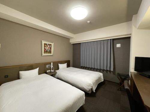 a hotel room with two beds and a flat screen tv at Hotel Route-Inn Ina Inter in Minamiminowa