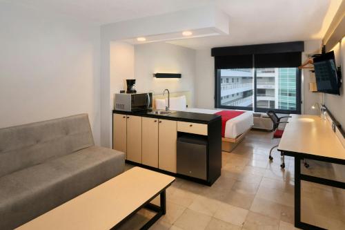 a small hotel room with a bed and a couch at City Express by Marriott Cancun in Cancún