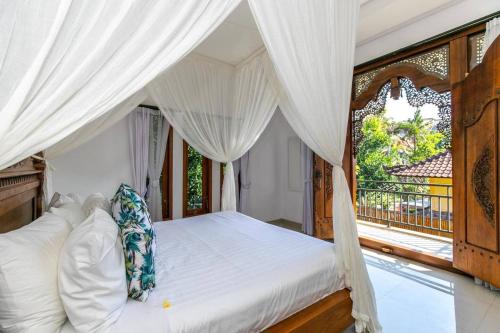 a bedroom with a bed with white curtains and a window at Villa Aniela Legian in Legian