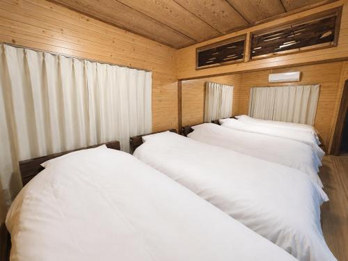 two white beds in a room with wooden walls at Hav Living in Oshima
