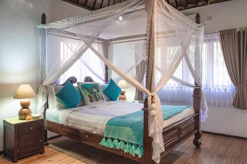 a bedroom with a canopy bed with blue pillows at Villa Karma Legian in Legian