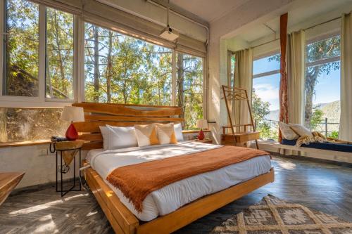 a bedroom with a large bed and large windows at Seclude Ramgarh Cliff's edge in Rāmgarh