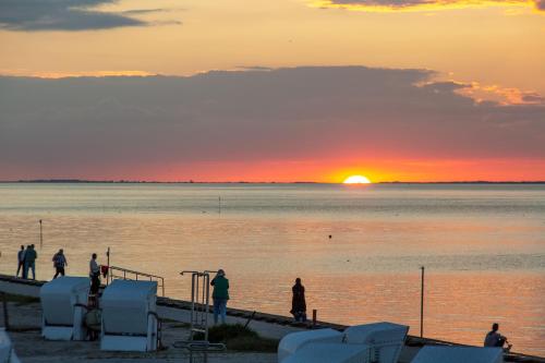 a group of people standing on a dock at sunset at 216 große Ferienwohnung Schwalbennest in Wittmund