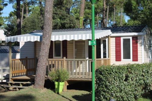 une petite maison avec une véranda et un arbre dans l'établissement Mobil-home 4 pers dans Camping 4 étoiles La Palmyre, à La Palmyre