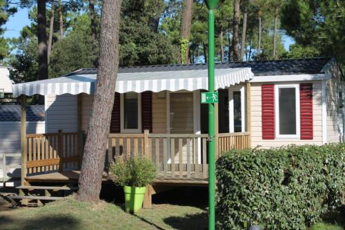 a small house with a porch and a tree at Mobil-home 4 pers dans Camping 4 étoiles La Palmyre in La Palmyre