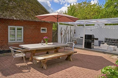 a picnic table with a bench and an umbrella at Reetdachhaus De Ole Kaat in Niesgrau