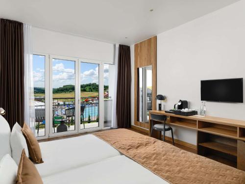 a hotel room with a bed and a desk with a television at Movenpick Resort and Spa Fruske Terme in Vrdnik