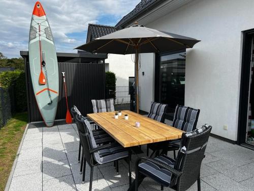 a wooden table with chairs and an umbrella and a surfboard at Villa Seeblick am Fleesensee in Göhren-Lebbin