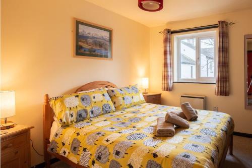 a bedroom with a bed with a yellow comforter and a window at Green Beck Cottage, within walking distance of the lake, shops, pubs & restaurants of Coniston in Coniston