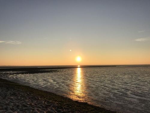 a sunset over the water with the sun in the sky at Ferienwohnung Landliebe in Süderschweiburg