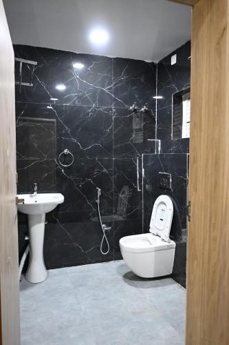 a black tiled bathroom with a toilet and a sink at Hota Residency in Sonepur