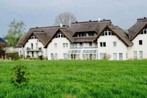a large white house with a large field of green grass at Fewo 18 im Strandhaus Lobbe mit Balkon in Lobbe