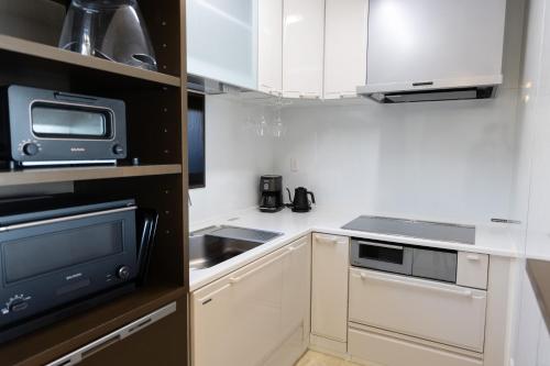 a small kitchen with white cabinets and a microwave at Nesoberi VILLA TAKASU in Kanoya
