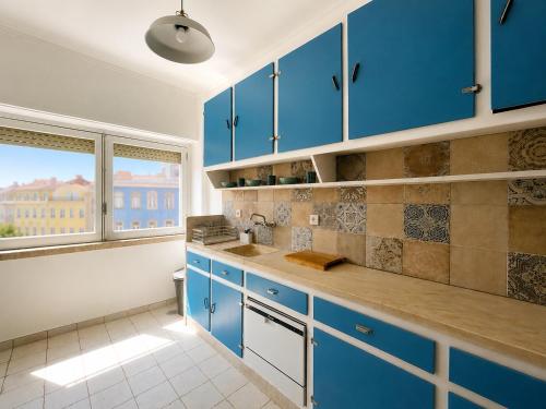 a kitchen with blue cabinets and a window at Lx Factory Apartment-Lisbon Style-Spacious & Bright-Congress Centre in Lisbon