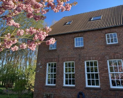 a brick house with white windows and a flowering tree at Gulfhof Friedrichsgroden in Carolinensiel