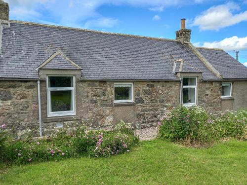 an old stone house with flowers in front of it at Benwells Holiday Cottage in Maud