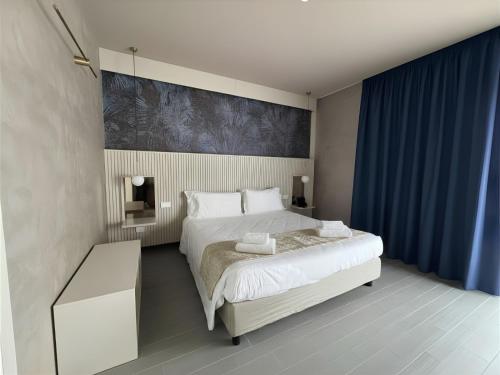 a bedroom with a large white bed and blue curtains at Hotel Kaos in Villaggio Pirandello