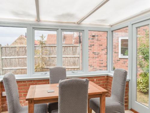 a dining room with windows and a wooden table and chairs at The Old Paybarn - Uk39378 in Snettisham