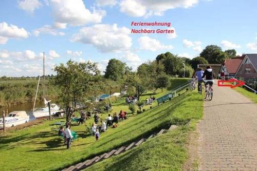 a group of people sitting on the grass near a river at Ferienwohnung Nachbars Garten in Grünendeich