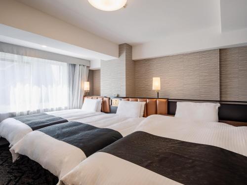 a hotel room with three beds and a window at APA Hotel Sapporo Odori Ekimae Minami in Sapporo