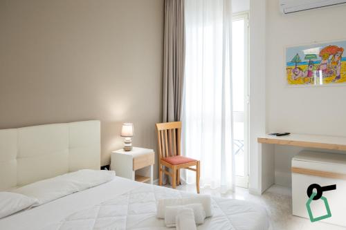 a white bedroom with a bed and a chair at Hotiday Porto Cesareo in Porto Cesareo